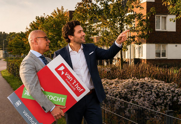 Twee makelaars wijzen in de verte, waarvan één makelaar een verkoopbord vasthoudt.